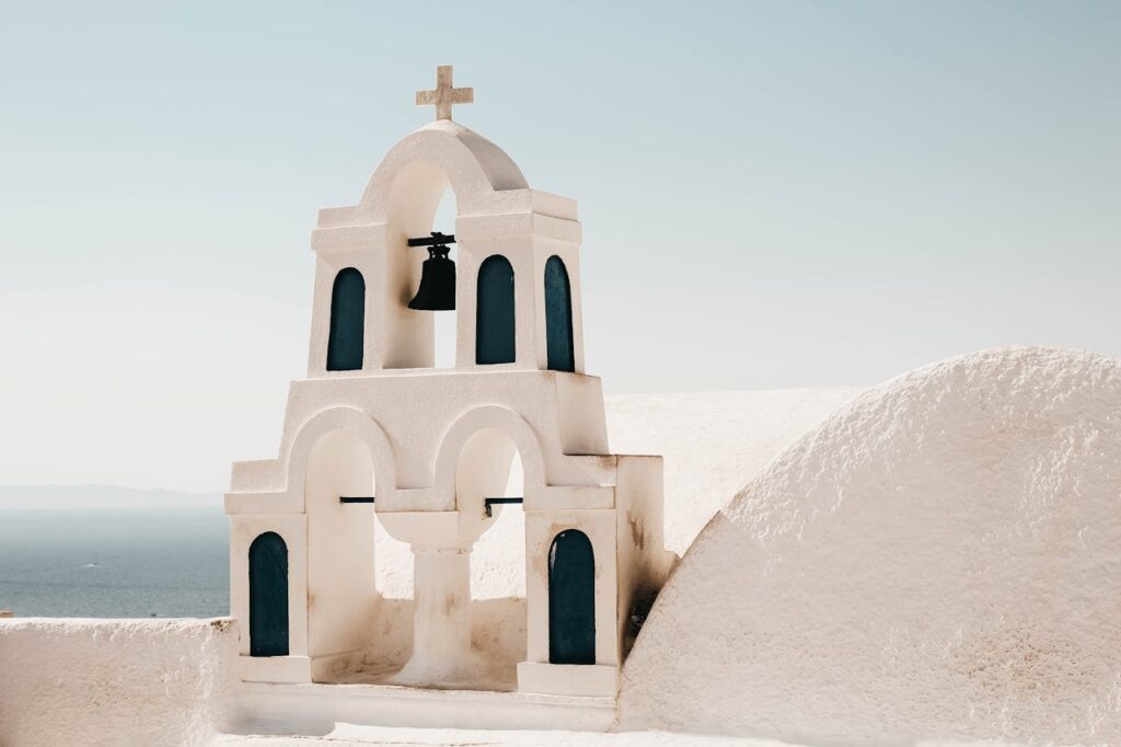 Iconic white church bell tower with cross under clear blue skies in Santorini, Greece.