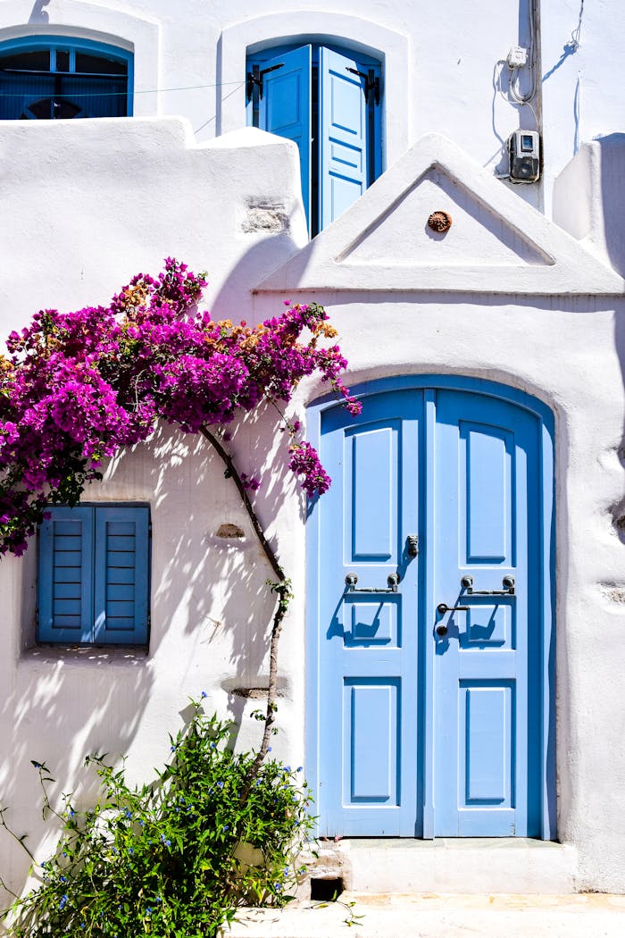 A picturesque Greek house facade with vibrant bougainvillea and blue doors and windows.